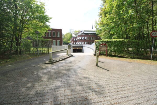 Ingang naar een ondergrondse parkeergarage bij een kantoorpand aan de Arnhemse Bovenweg, omgeven door bomen en groen.
